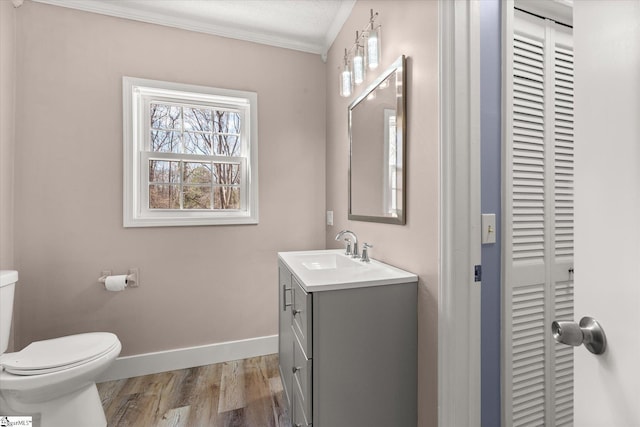 half bathroom featuring a closet, baseboards, wood finished floors, toilet, and vanity