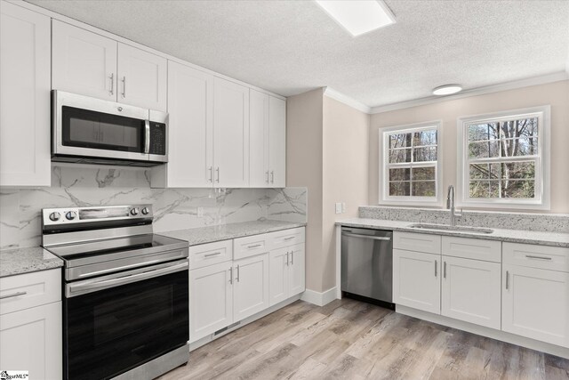 kitchen with a sink, backsplash, light wood finished floors, white cabinetry, and appliances with stainless steel finishes