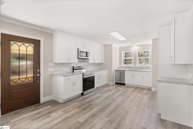 kitchen with a sink, light wood finished floors, white cabinetry, stainless steel appliances, and decorative backsplash