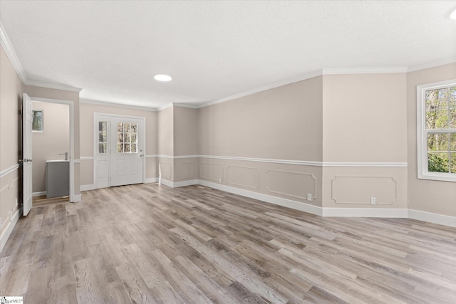 spare room with a textured ceiling, wood finished floors, crown molding, and wainscoting