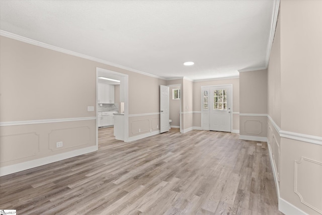 unfurnished room with ornamental molding, a decorative wall, light wood-style floors, and wainscoting