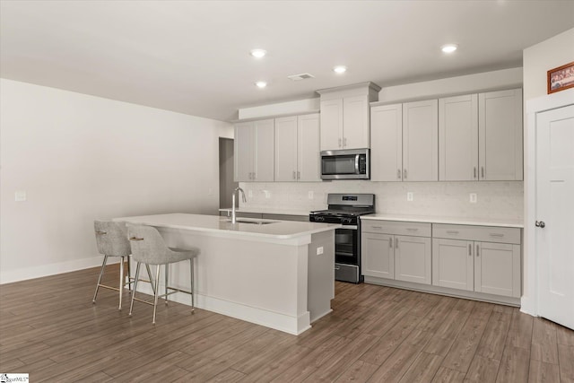kitchen featuring tasteful backsplash, a sink, an island with sink, appliances with stainless steel finishes, and wood finished floors