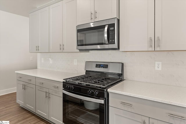 kitchen featuring tasteful backsplash, appliances with stainless steel finishes, light wood-style floors, and baseboards