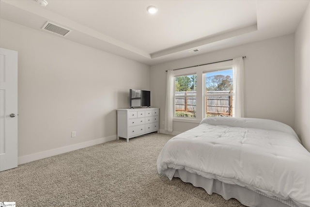 carpeted bedroom featuring a tray ceiling, baseboards, and visible vents