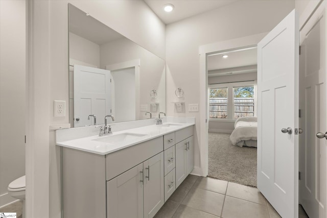 ensuite bathroom featuring toilet, a sink, double vanity, and tile patterned floors
