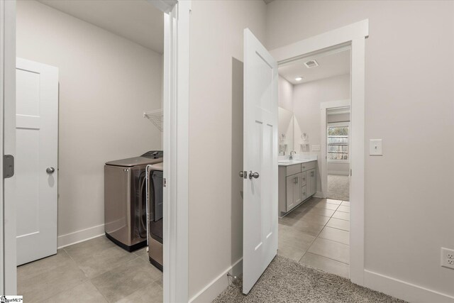 clothes washing area with baseboards, a sink, light carpet, washer and dryer, and laundry area