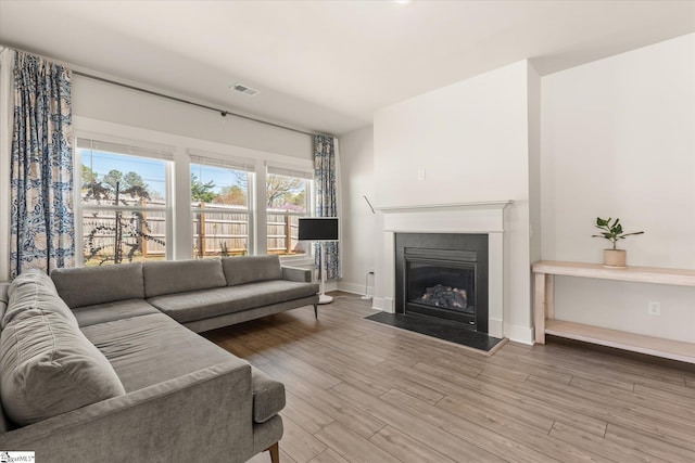 living room featuring a fireplace with flush hearth, baseboards, visible vents, and wood finished floors
