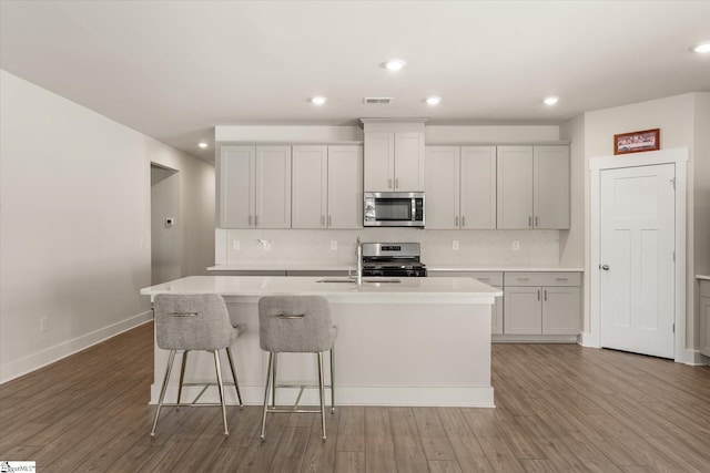 kitchen featuring an island with sink, light countertops, a sink, wood finished floors, and stainless steel appliances