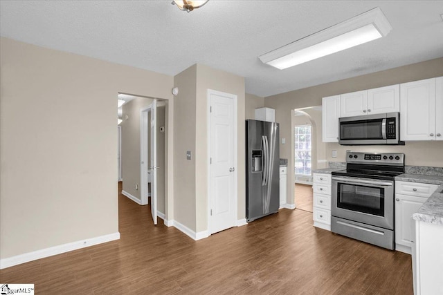 kitchen with dark wood-style flooring, white cabinets, baseboards, stainless steel appliances, and arched walkways
