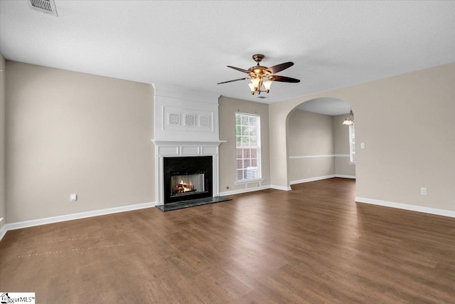 unfurnished living room with arched walkways, visible vents, a ceiling fan, a fireplace, and wood finished floors