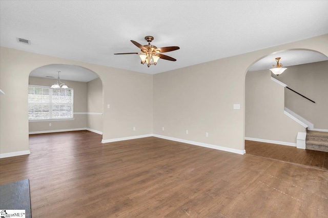 unfurnished living room featuring ceiling fan with notable chandelier, visible vents, wood finished floors, and baseboards