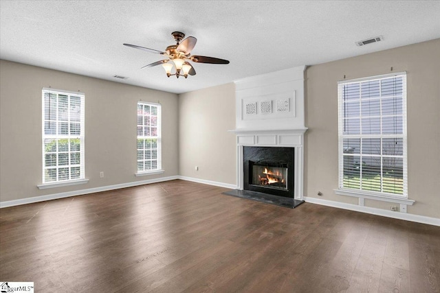 unfurnished living room featuring a textured ceiling, visible vents, a fireplace, a ceiling fan, and dark wood-style floors