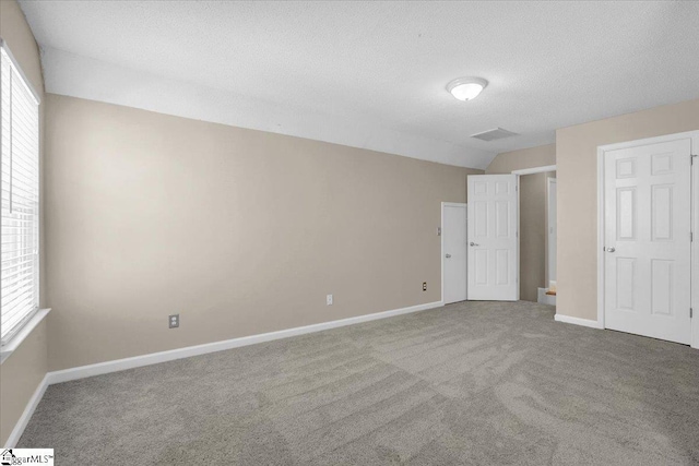 unfurnished bedroom with baseboards, lofted ceiling, a textured ceiling, and carpet