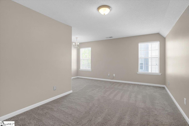 carpeted empty room with a textured ceiling, baseboards, and a chandelier