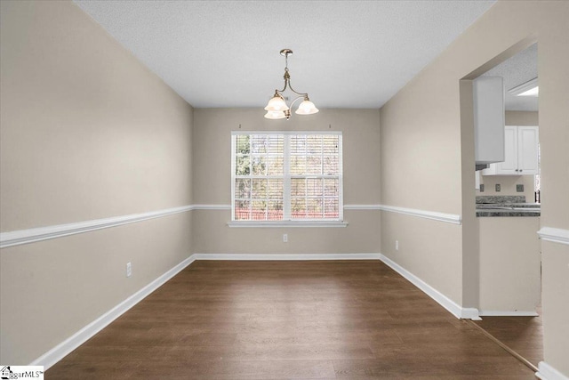 unfurnished dining area featuring baseboards, a textured ceiling, dark wood-style floors, and a chandelier