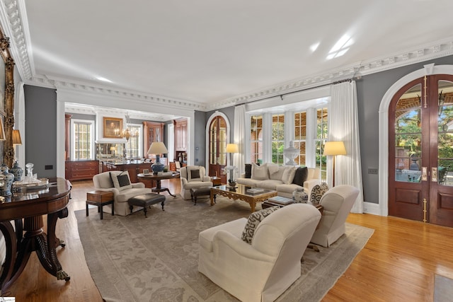 living area featuring french doors, light wood-style flooring, ornamental molding, and an inviting chandelier