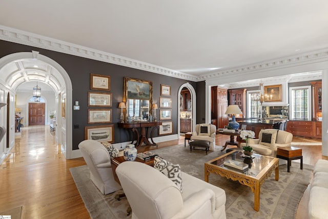 living area with arched walkways, an inviting chandelier, light wood-style floors, and crown molding