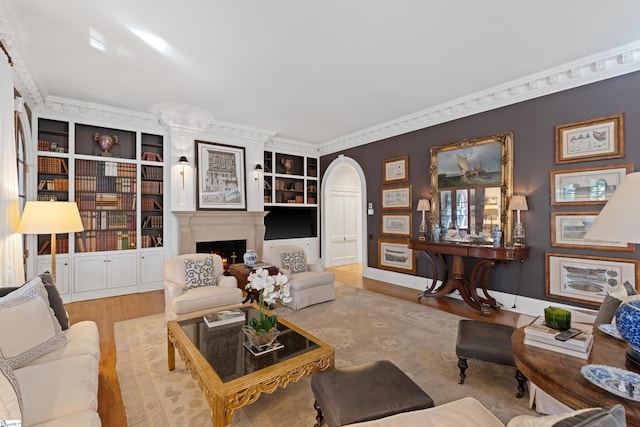 living room featuring a warm lit fireplace, baseboards, ornamental molding, wood finished floors, and arched walkways