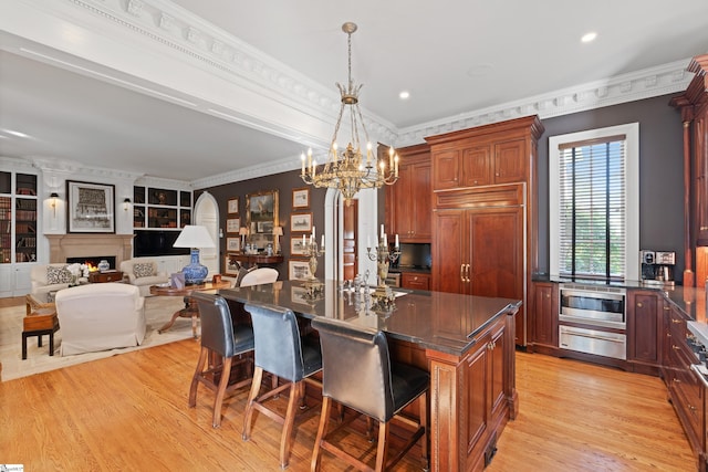 kitchen featuring stainless steel microwave, light wood-type flooring, a warming drawer, a kitchen breakfast bar, and a notable chandelier
