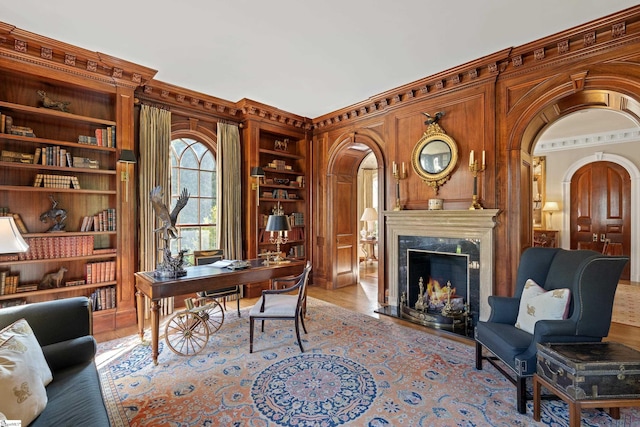 office with crown molding, light wood-type flooring, arched walkways, built in features, and a fireplace