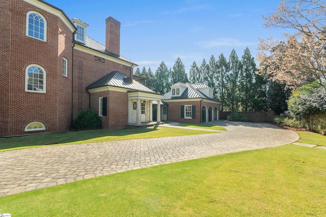 rear view of house with brick siding, decorative driveway, a standing seam roof, and a lawn