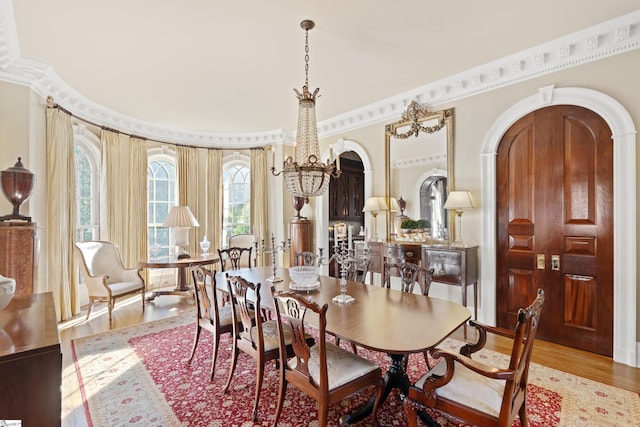 dining room featuring ornamental molding, arched walkways, a chandelier, and wood finished floors