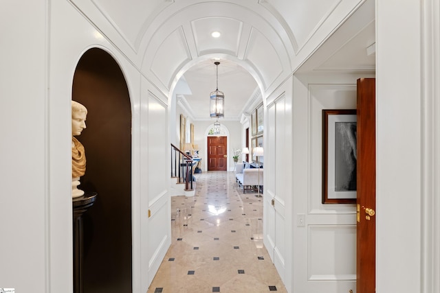 hall featuring crown molding, vaulted ceiling, stairs, arched walkways, and a decorative wall