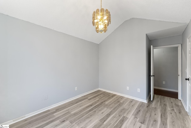 spare room featuring light wood finished floors, baseboards, a notable chandelier, and vaulted ceiling