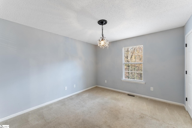 carpeted spare room with a notable chandelier, a textured ceiling, baseboards, and visible vents
