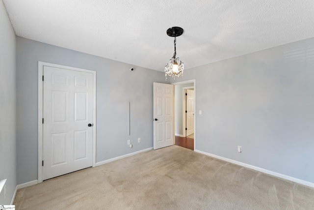 unfurnished room featuring light carpet, baseboards, a notable chandelier, and a textured ceiling