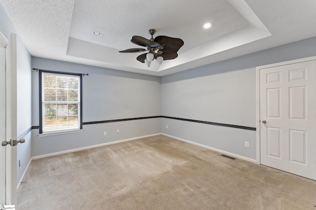 unfurnished room with a textured ceiling, a raised ceiling, carpet floors, ceiling fan, and visible vents