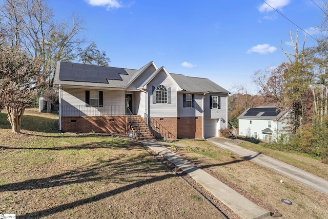 view of front of property featuring covered porch, concrete driveway, an attached garage, a front lawn, and solar panels