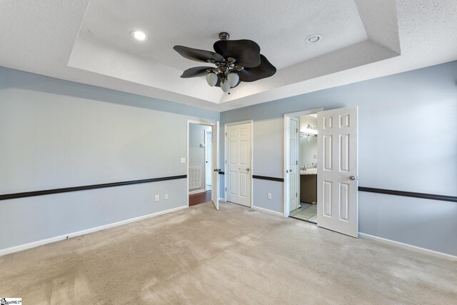 unfurnished bedroom featuring light carpet, baseboards, a textured ceiling, and a raised ceiling