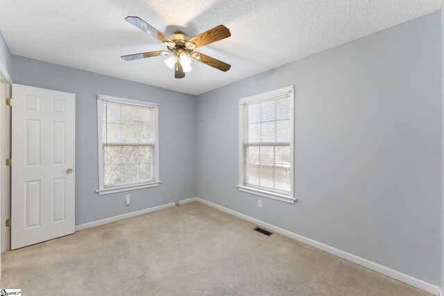 carpeted spare room featuring a wealth of natural light, visible vents, a textured ceiling, and a ceiling fan