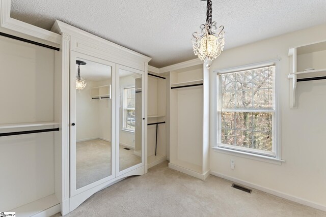 unfurnished bedroom featuring two closets, an inviting chandelier, a textured ceiling, carpet floors, and visible vents