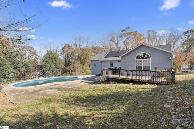 rear view of property with a wooden deck, roof mounted solar panels, an outdoor pool, a patio, and a lawn
