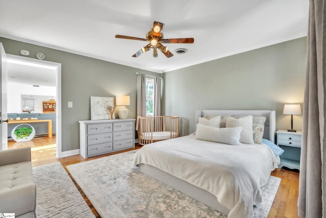 bedroom with baseboards, visible vents, wood finished floors, and crown molding