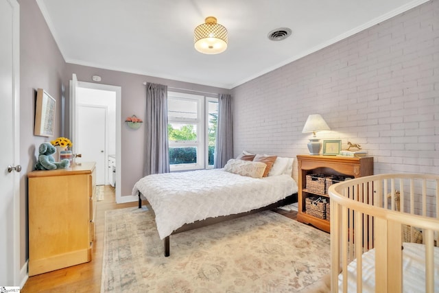 bedroom featuring visible vents, crown molding, baseboards, light wood-style floors, and brick wall
