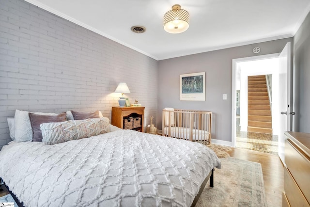 bedroom with ornamental molding, baseboards, brick wall, visible vents, and wood finished floors
