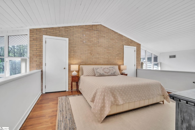 bedroom with vaulted ceiling, baseboards, brick wall, visible vents, and wood finished floors