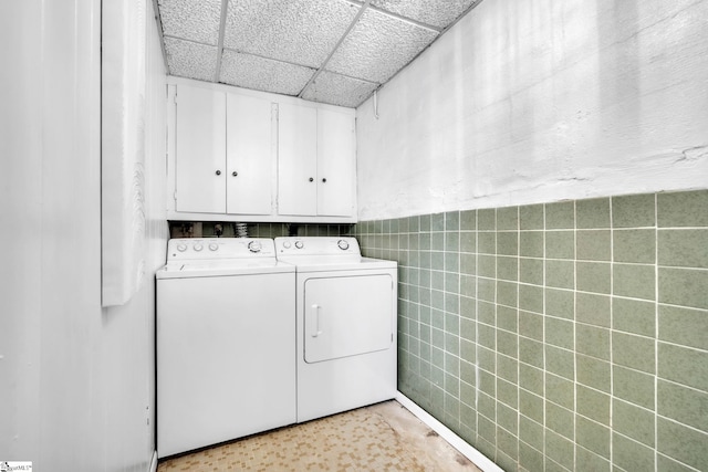 clothes washing area featuring washing machine and clothes dryer, cabinet space, tile walls, and a wainscoted wall