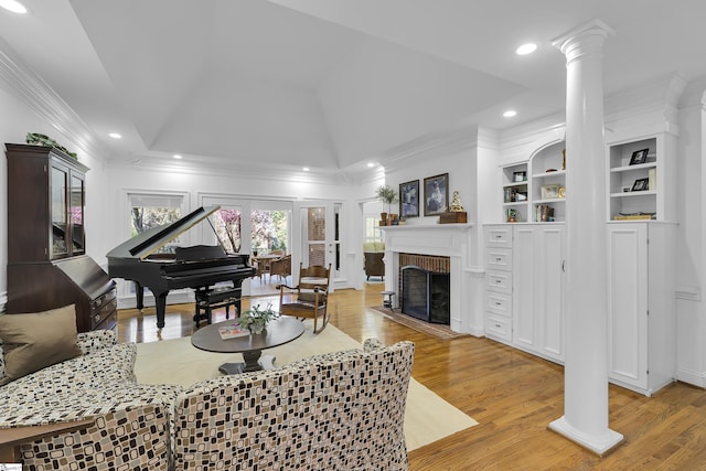 living room with ornate columns, a brick fireplace, crown molding, and light wood finished floors