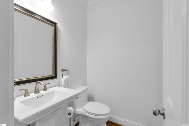 bathroom with baseboards, crown molding, toilet, and a sink
