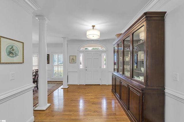 foyer entrance featuring ornamental molding, light wood-type flooring, a decorative wall, and decorative columns