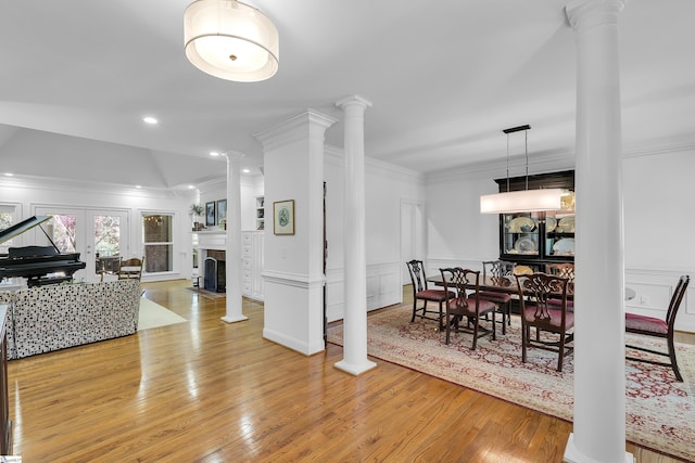 dining room with a decorative wall, crown molding, light wood-style floors, and decorative columns