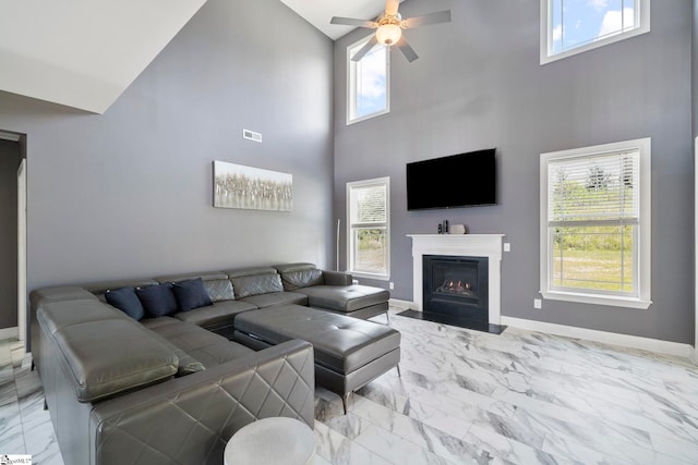 living area with a ceiling fan, marble finish floor, a fireplace with flush hearth, and baseboards