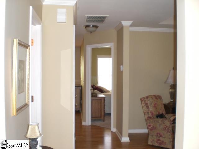 hallway featuring baseboards, visible vents, crown molding, and wood finished floors