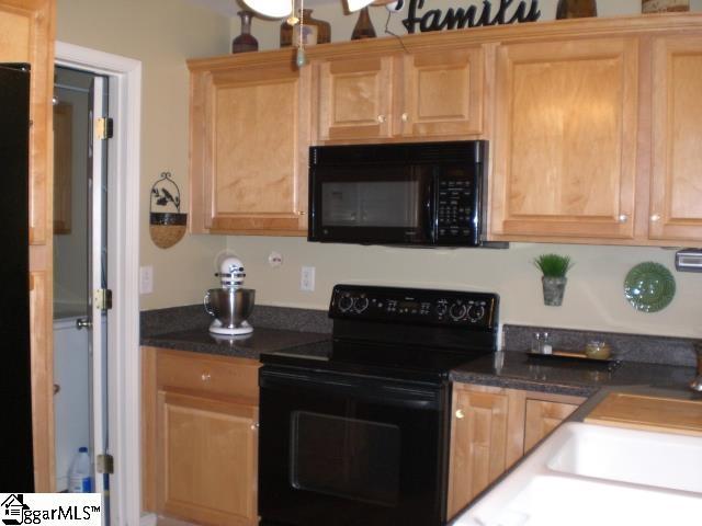 kitchen featuring a sink, dark countertops, light brown cabinetry, and black appliances