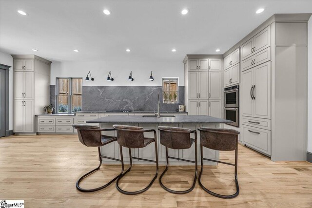 kitchen with a sink, double oven, a kitchen breakfast bar, gray cabinetry, and dark countertops