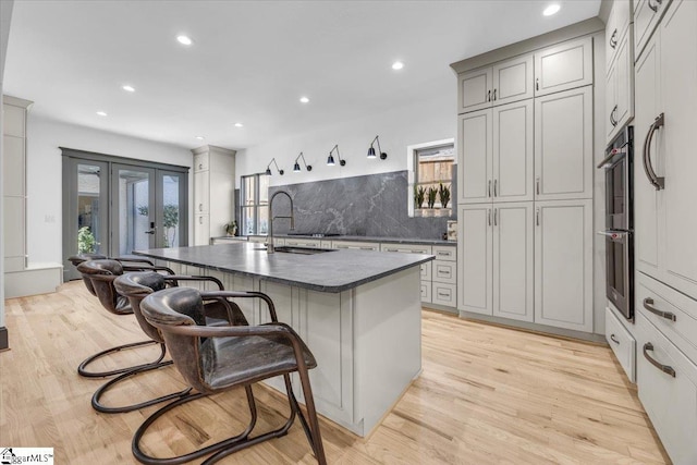 kitchen featuring tasteful backsplash, a breakfast bar area, french doors, dark countertops, and light wood finished floors